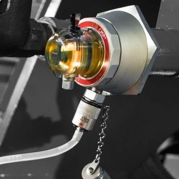 Luneta Condition Monitoring Pod on a machine port, with amber oil visible through its clear body