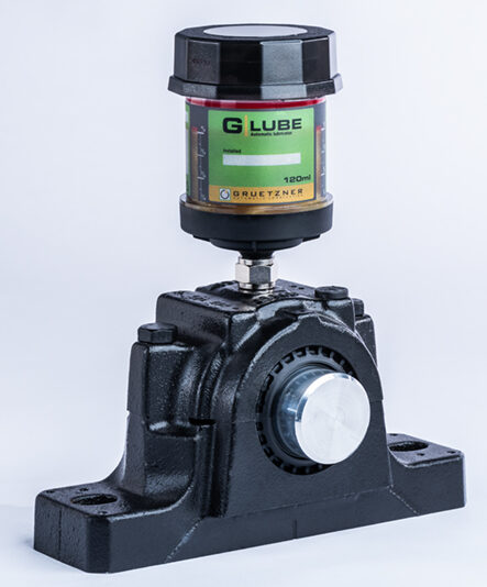 G-LUBE 120 ml automatic lubricator screwed through a short connector into the top of a black plummer-block bearing housing